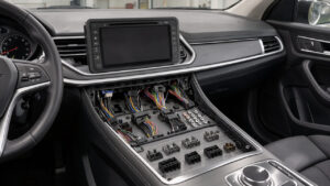 Intérieur de voiture moderne avec la console centrale démontée, un écran tactile vierge et des faisceaux électriques visibles dans un environnement technique.